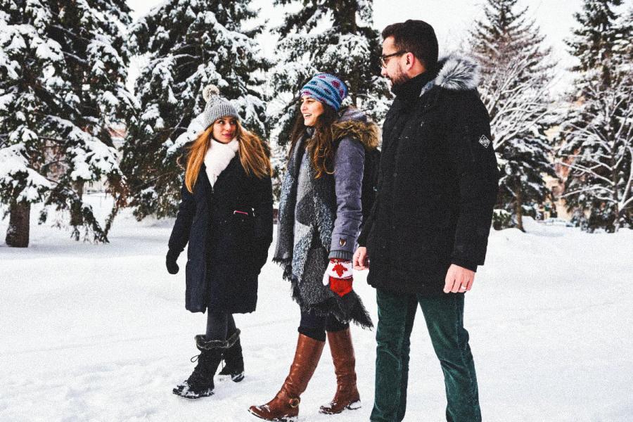 An image of three students walking, talking and smiling outside on a winter day.