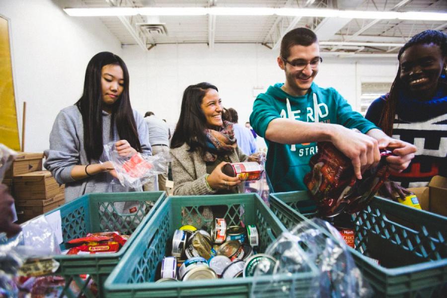 An image of a few people laughing and smiling together while working at a food drive.
