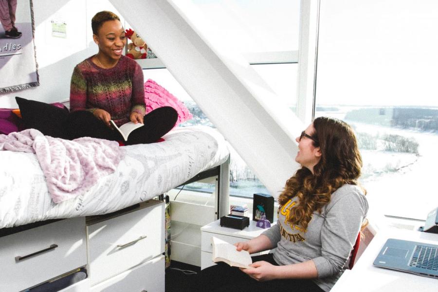 An image of two students in residence, one sitting on the bed, the other sitting on a chair, conversing together.