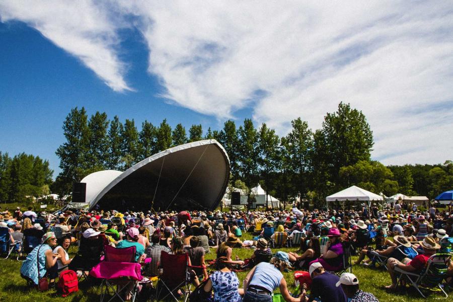 A crowd of people sitting outside watching one of the stages at the Winnipeg Folk Fest.