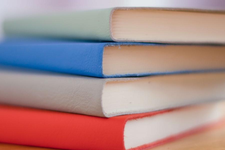 A stack of leather bound books on a wood desk