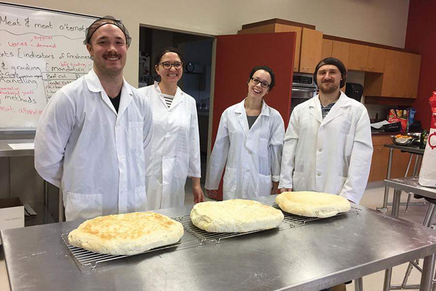 Four students in the Slater lab standing behind a kitchen table with dough on it.