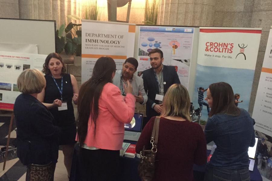 A group of people stand at a Department of Immunology booth talking to graduate program representatives.