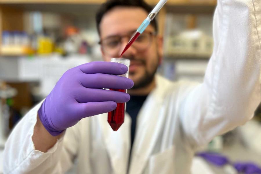 A researcher in a white lab uses an eyedropper to drop blood into a vial.