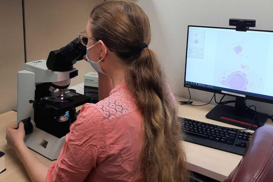 A researcher looks at slides under a microscope, which displays data on the computer screen next to her.