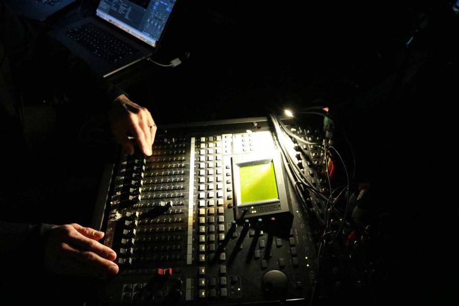 close-up of a person's hands adjusting the slider levels on a soundboard.