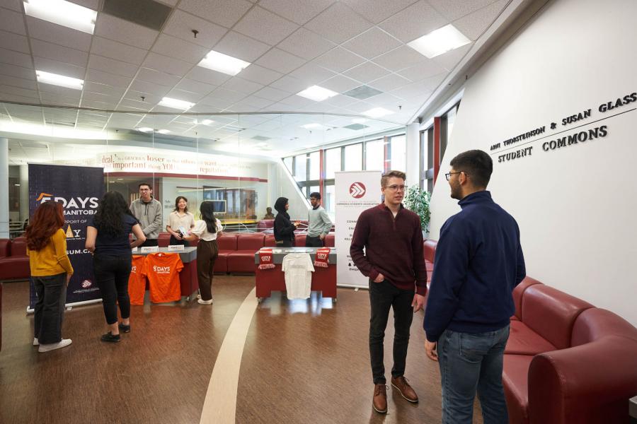 Nine students stand in groups talking in the Drake Centre Arni Thorsteinson and Susan Glass student commons.