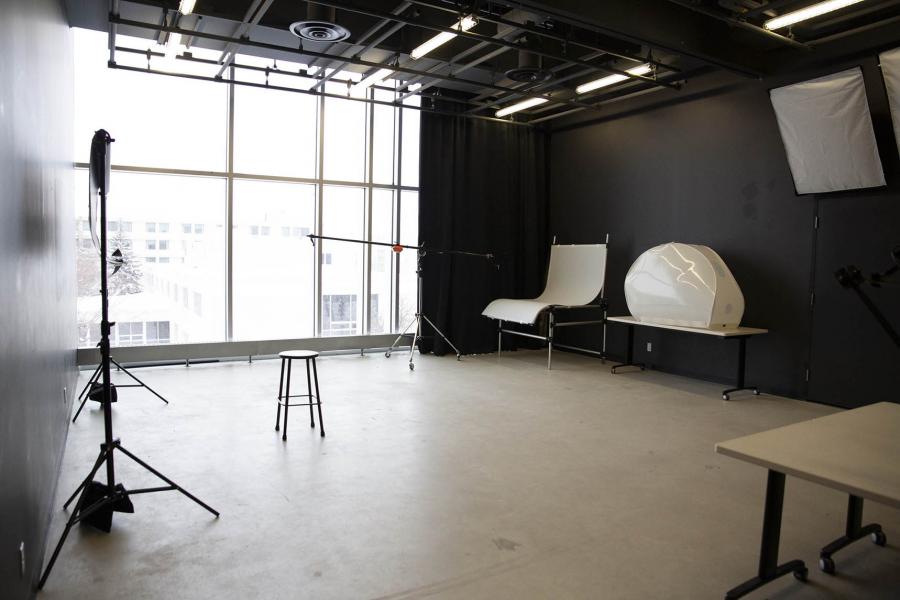 A photo studio room with black walls and photo equipment is lit by a wide window on the outside wall.