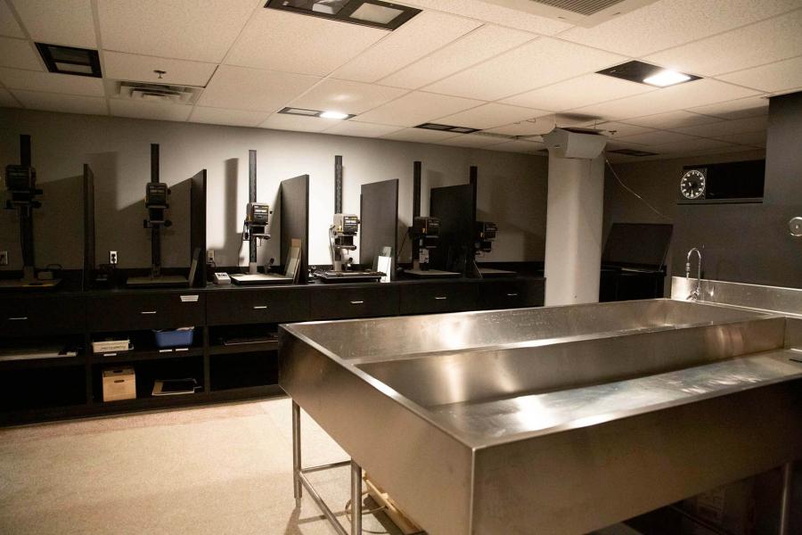 A dimly lit room for developing photos with a large metal dual sink in the foreground.