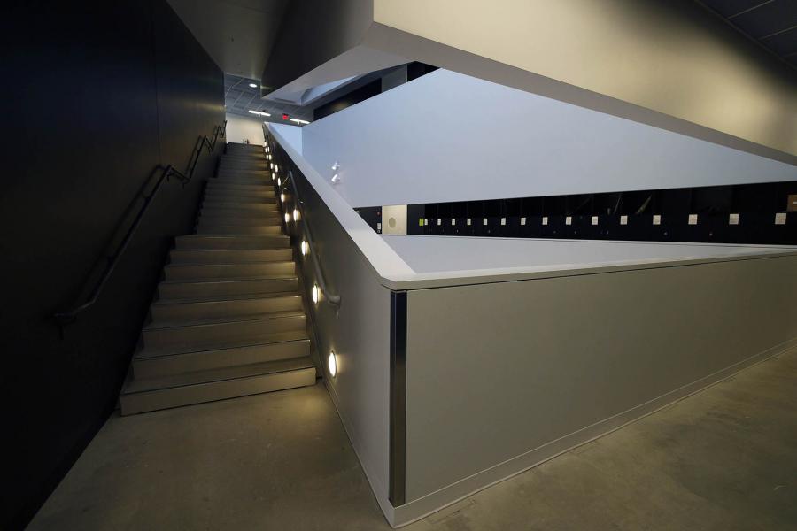 A black and white stairway going upwards is lit by circular floor lights near each step.