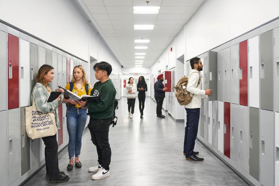 Asper School of Business students walk down a hallway of gray, white and red lockers in the Drake Centre.