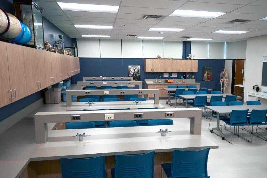  A classroom with blue walls is filled with gray tables with blue chairs facing each other in the Education Building.