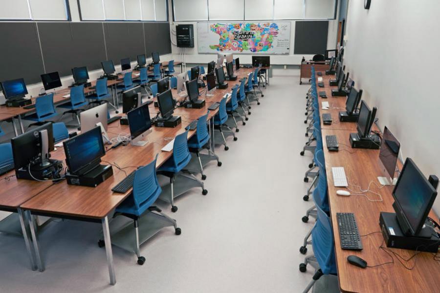 An Education Building classroom is filled with computers and monitors in columns of wooden tables.