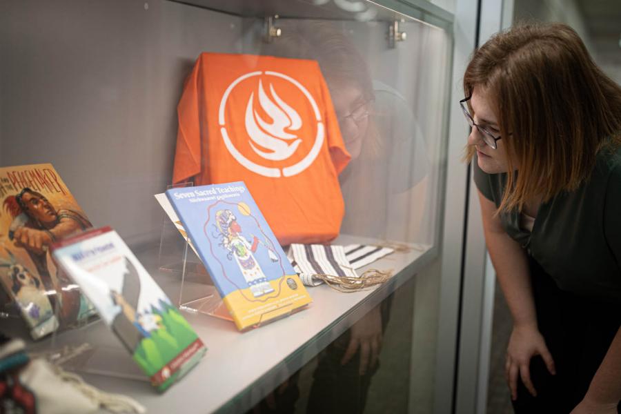 A person stands in front of a glass display case filled with early education books on Indigenous teachings.