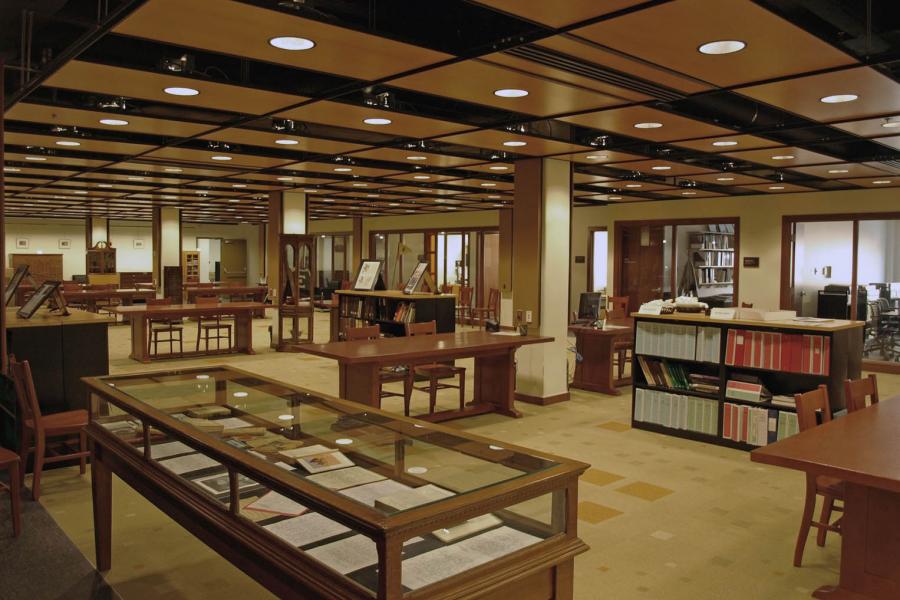 An Elizabeth Dafoe Library room shows archives of books behind glass displays and wooden tables with chairs.