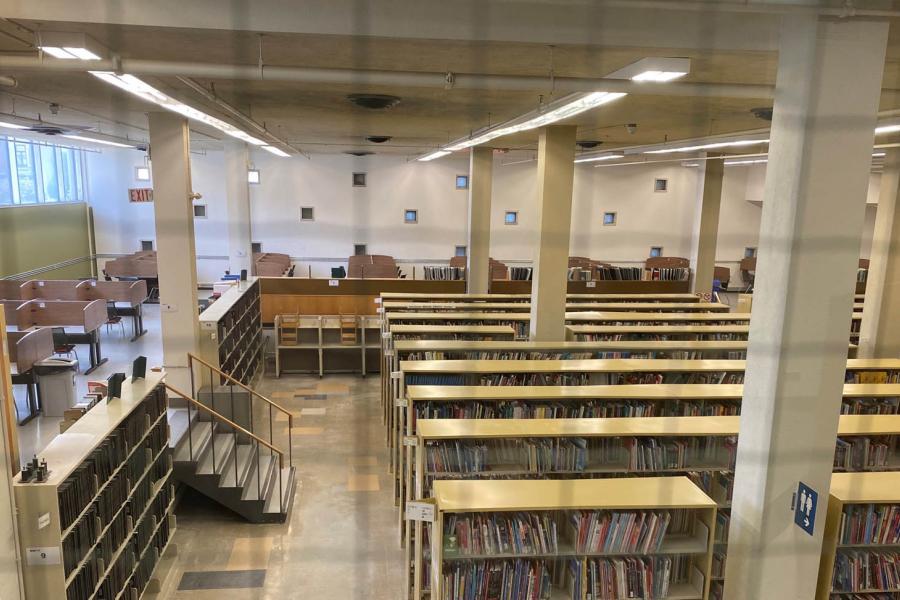 Aisles of shelves with books are surrounded by a perimeter of tables with walls for studying at the Elizabeth Dafoe Library.