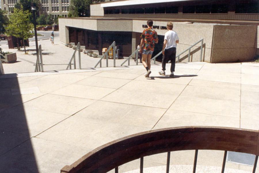 Two people walk outside towards the stairs going away from the entrance of the Elizabeth Dafoe Library.