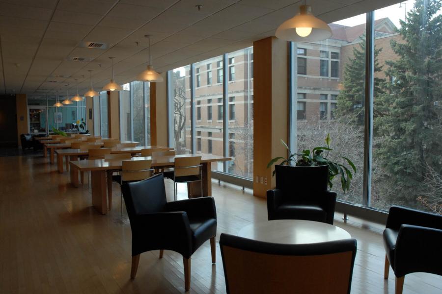 A row of tables and chairs are lined up against a large window in a comfortable looking study area at the Elizabeth Dafoe Library.