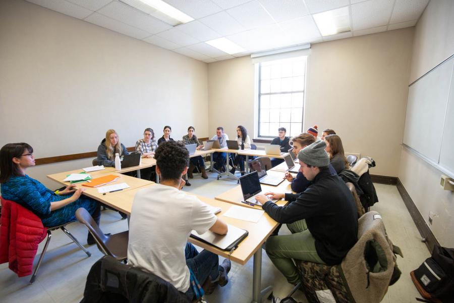 A classroom of students sit facing each other at tables in a square in the Fletcher Argue Building.