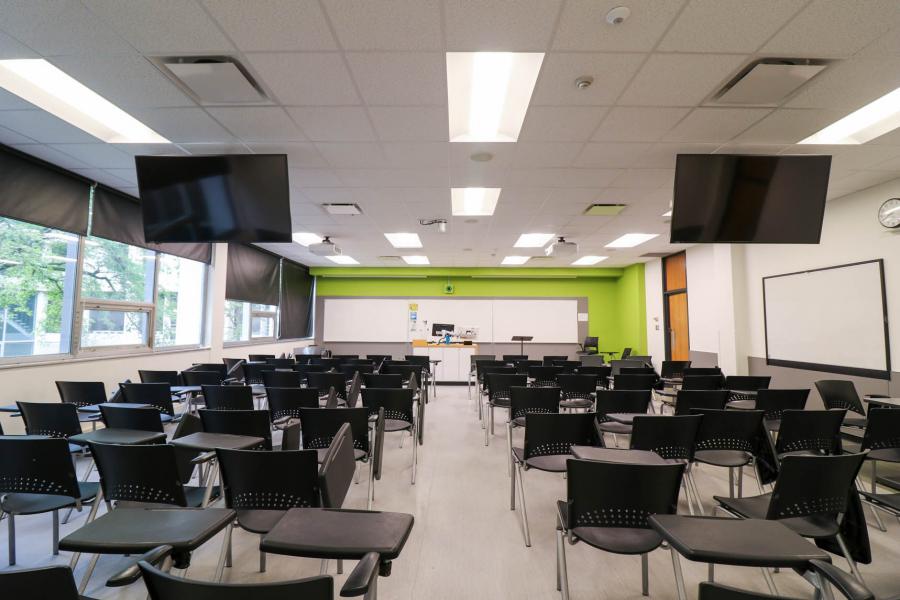 An empty classroom with black chairs facing two screens in the Fletcher Argue Building.