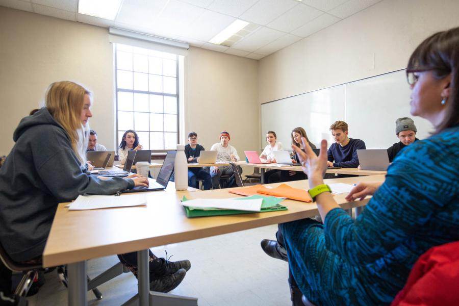 Students sit facing each other in a square of four tables in a Fletcher Argue Building classroom.