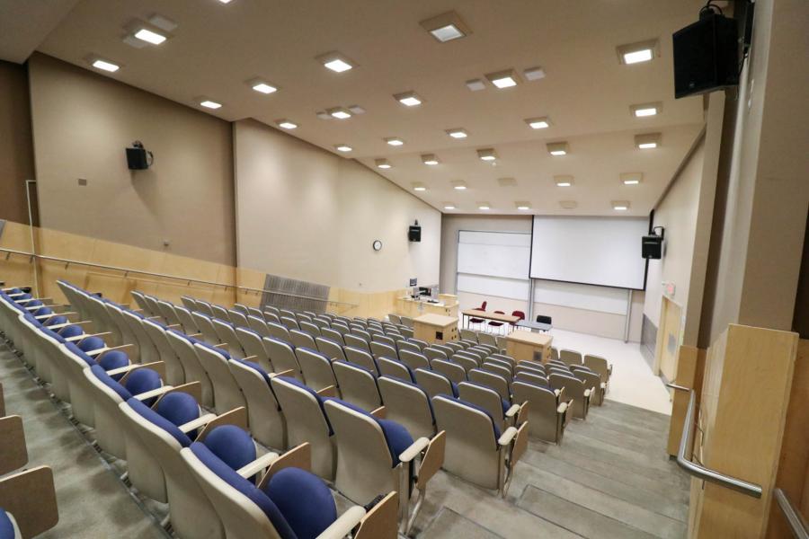 A large, empty lecture hall in the Fletcher Argue Building shows descending rows of blue theatre seats facing a podium below,