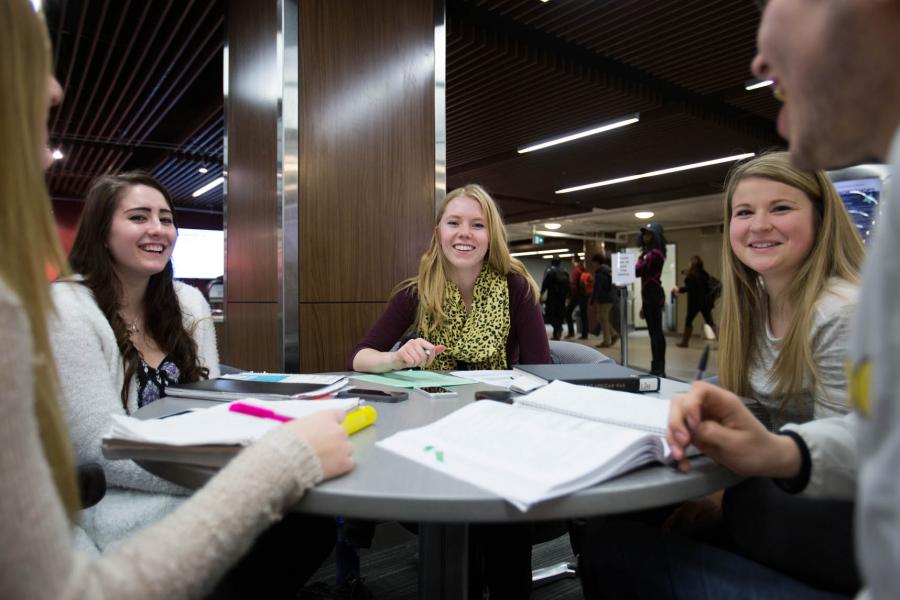 A group of students smile and laugh while studying at a round table in the Fletcher Argue Building.