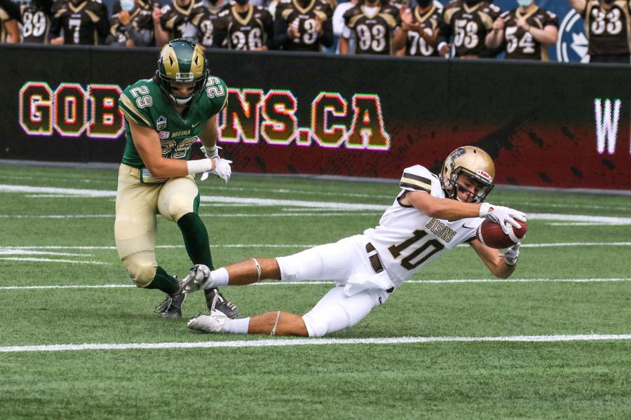 A University of Manitoba Bisons football player dives forward with the football on the playing field of the IG Field.