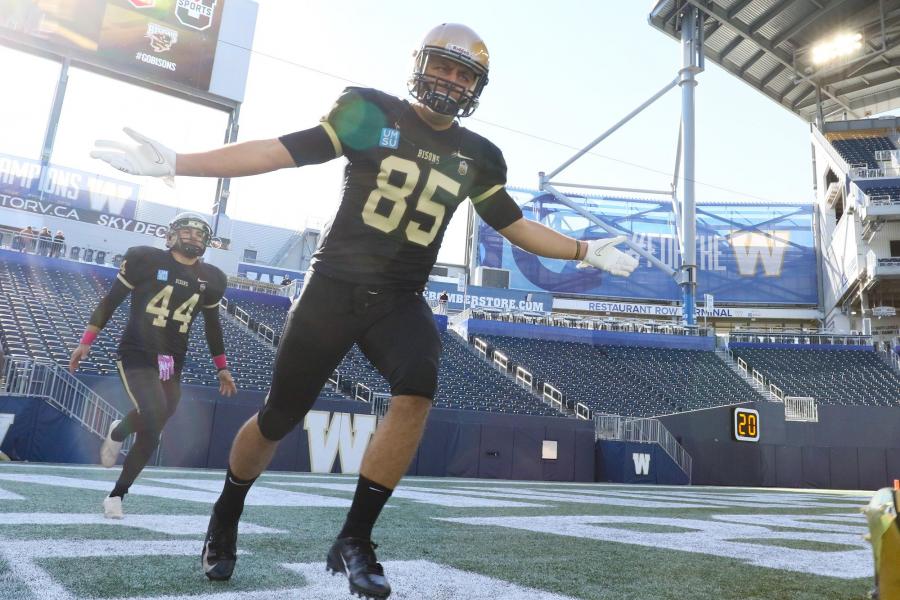 A University of Manitoba Bisons football player runs down IG Field with their arms spread widely.