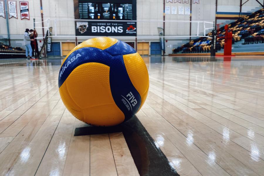 A close up of a yellow and blue volleyball placed on the ground of the UM Bisons Investors Group Athletic Centre volleyball court.