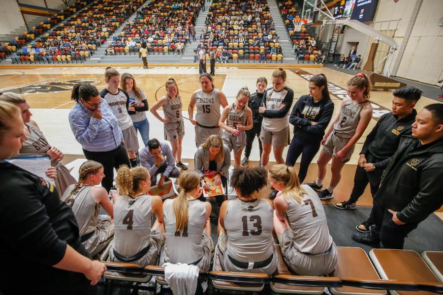 The UM Bisons women's basketball team huddles around a coach that is drawing a play during a game at the Investors Group Athletic Centre.