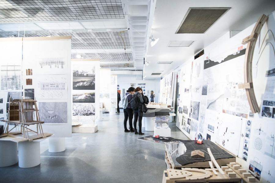Students walk through a brightly lit room in the John A. Russell Building that has many drawings and schematic designs on the walls and tables.