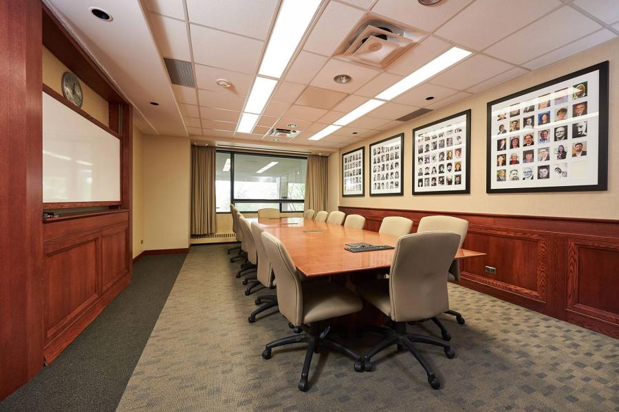 A boardroom at Robson Hall with a long wooden conference table in the middle and four groups of photos in frames on the wall.