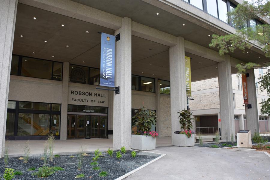 The exterior entry way to the Robson Hall Faculty of Law building with stone columns and glass doors under an overhang from the tall building.