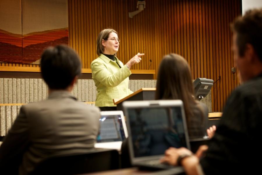 A Faculty of Law instructor wearing a green blazer speaks to a class of students using laptops in a Robson Hall classroom.