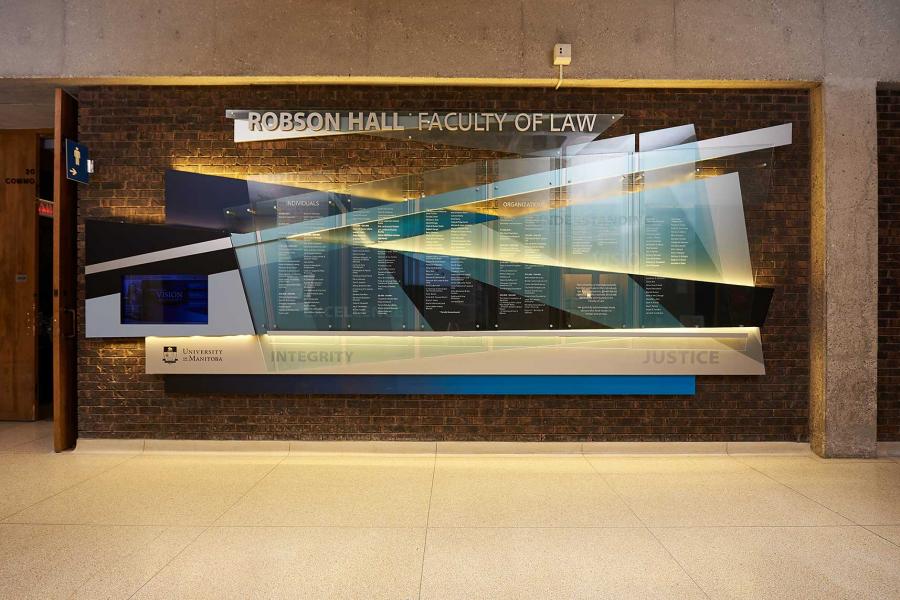 A glass board of overlapping blue, white, and transparent pieces of glass lists individual and group donors to the Faculty of Law Robson Hall.