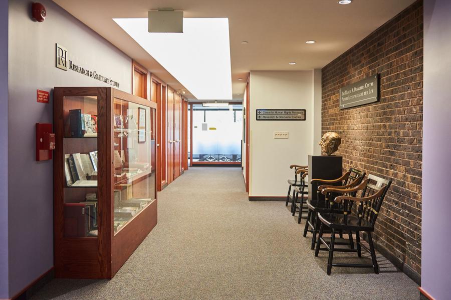 A hallway in the Faculty of Law Robson Hall with purple walls and brown bricks. Signs on the wall say Research and Graduate Studies.