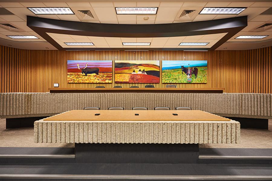 A stone sitting area with five seats in front of three colourful murals in Robson Hall.