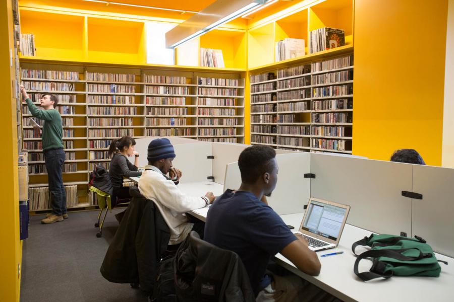 A yellow room at the Taché Arts Complex displays high shelves of books and white cubicles for studying in.