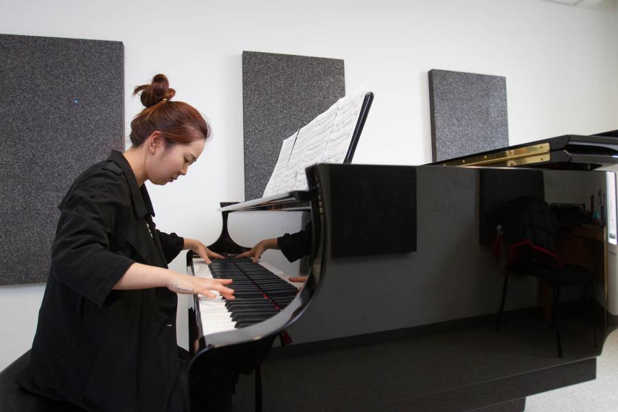 A close up of a musician seated at a black piano plays in the University of Manitoba Taché Arts Complex.