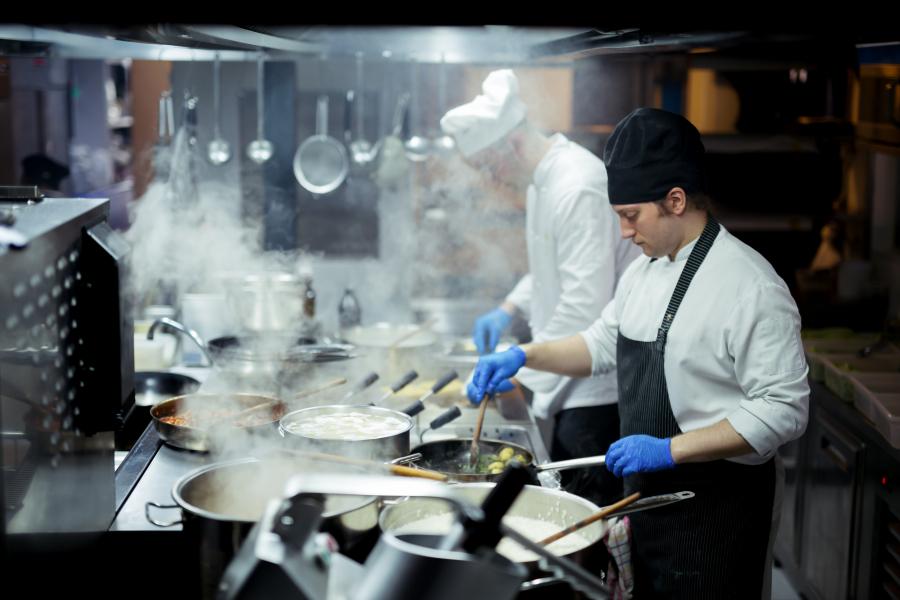 Chef in restaurant kitchen standing over a stove with steam rising from the pots and pans.
