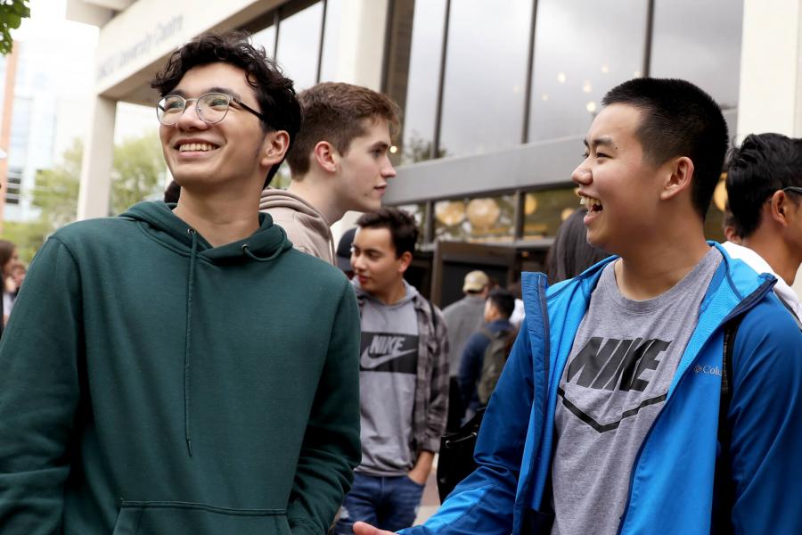 Two smiling students in a large group on campus.