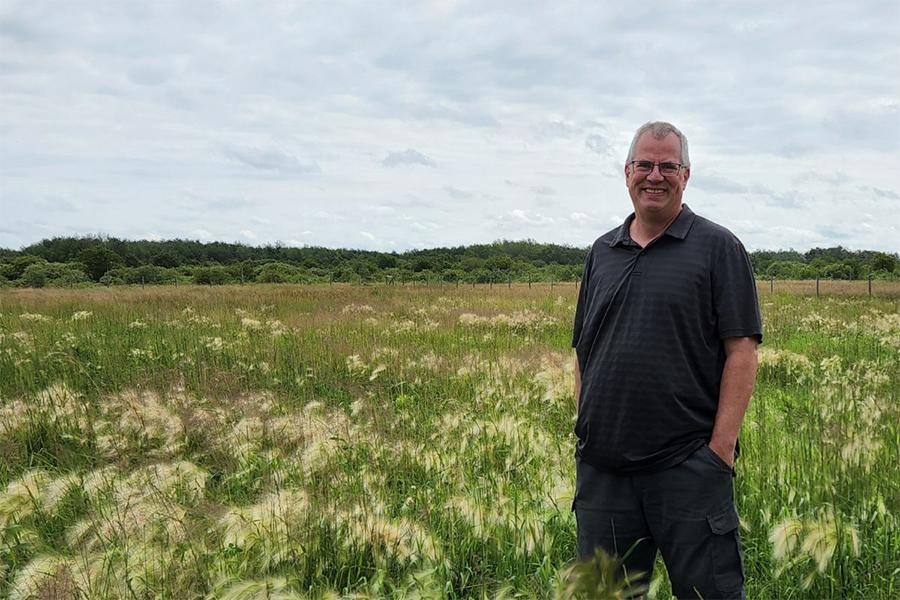 Asper professor Bruno Dyck smiling and standing in a prairie field.