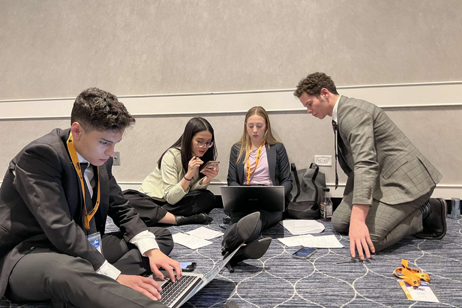 Asper students sitting on floor working on presentation, everyone is wearing business clothes.