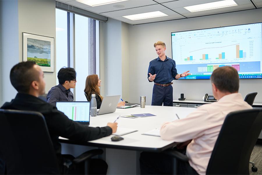 Asper co-op student standing at front of boardroom doing presentation.