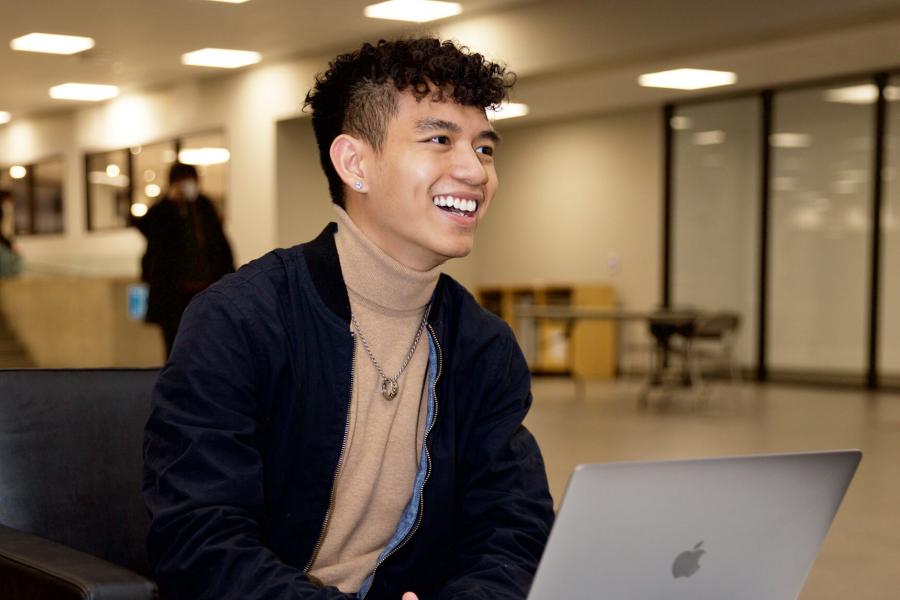 A smiling student sitting at a laptop.