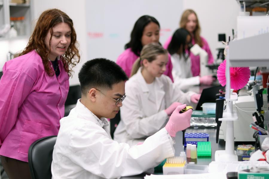 Students in a lab working on an experiment while mentors look on.