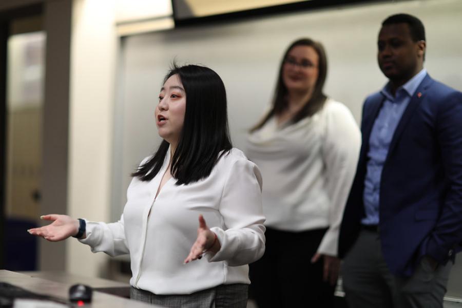 A student standing in front of two other people presenting to a room. 