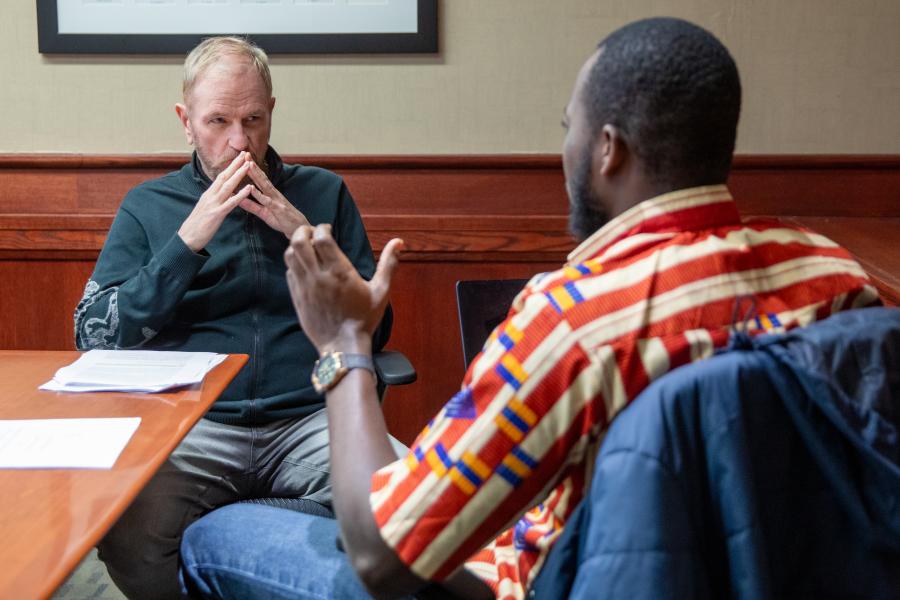 Student and advisor seated at a paper-strewn table having an animated and focused discussion.