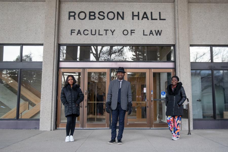 Three law grad students stand in front of the Robson Hall Faculty of Law entrance sign